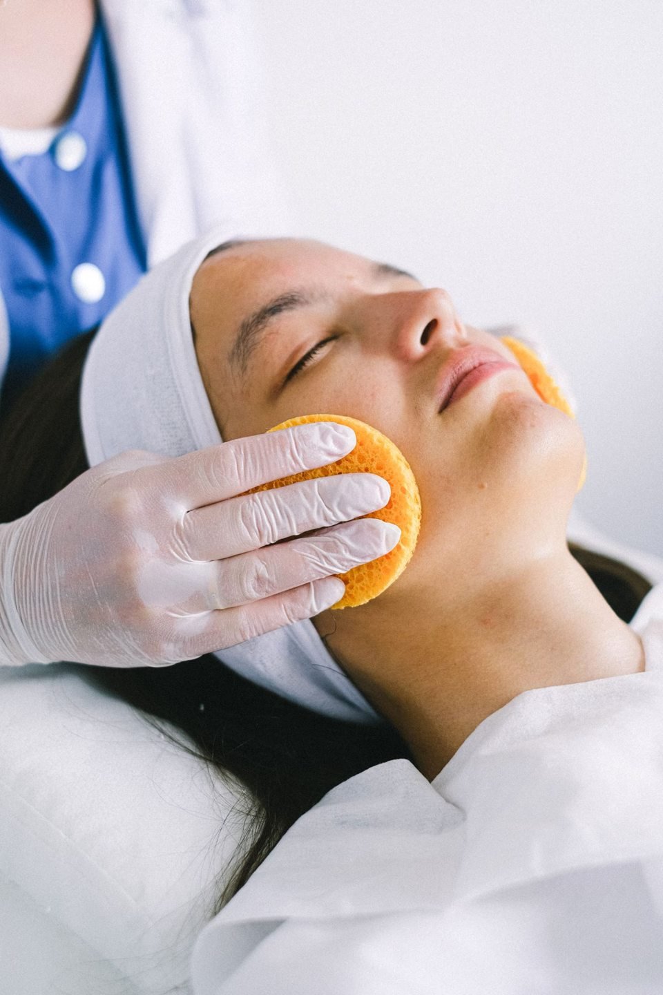Esthetician cleansing a client’s face with sponges